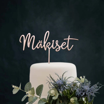 Puinen kakkukoriste hääkakkuun sukunimellä.